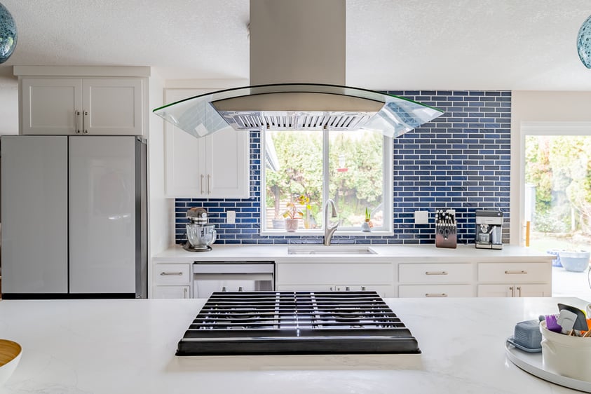 Large white quartz kitchen island with an integrated gas cooktop beneath a contemporary glass canopy range hood.