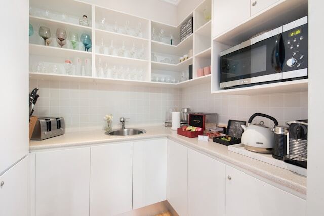 Scullery kitchen with shelving, a sink, microwave and other items